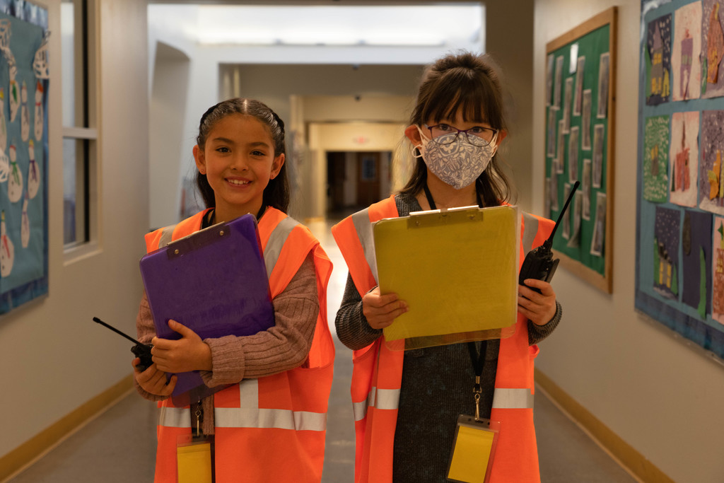 Two female students wearing reflective vests holding clipboards