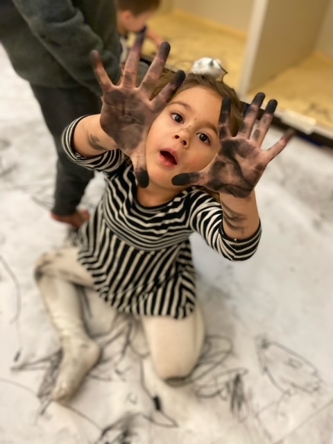 female toddler showing hands covered in charcoal dust