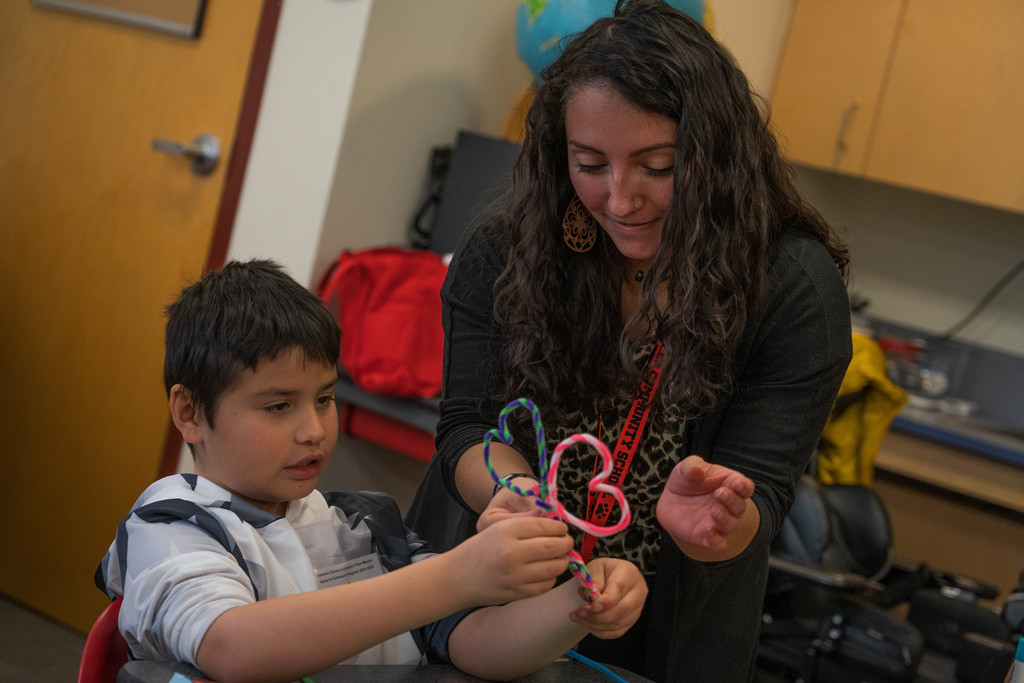 Teacher Ms. Gabby Kahawai holding pipecleaners for a male student