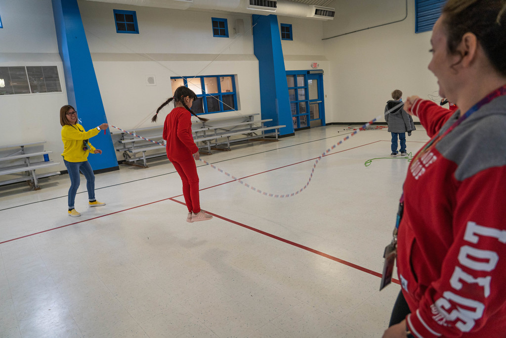 Female 5th grader jumping long rope with teacher in the background