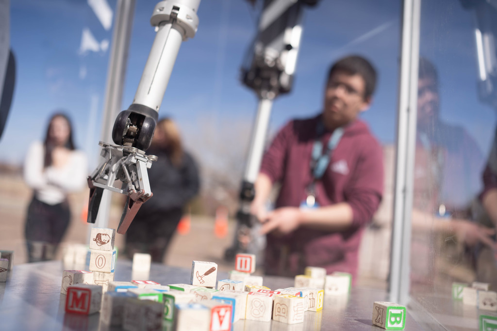 A robot arm stacking blocks with a student in the background
