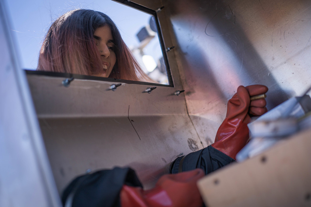 female student looking throuhg a window with gloves on handling material