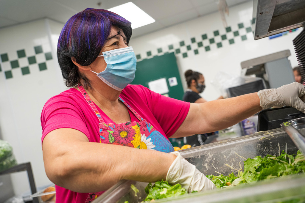 female student nutrition worker reaching for salad in a bin