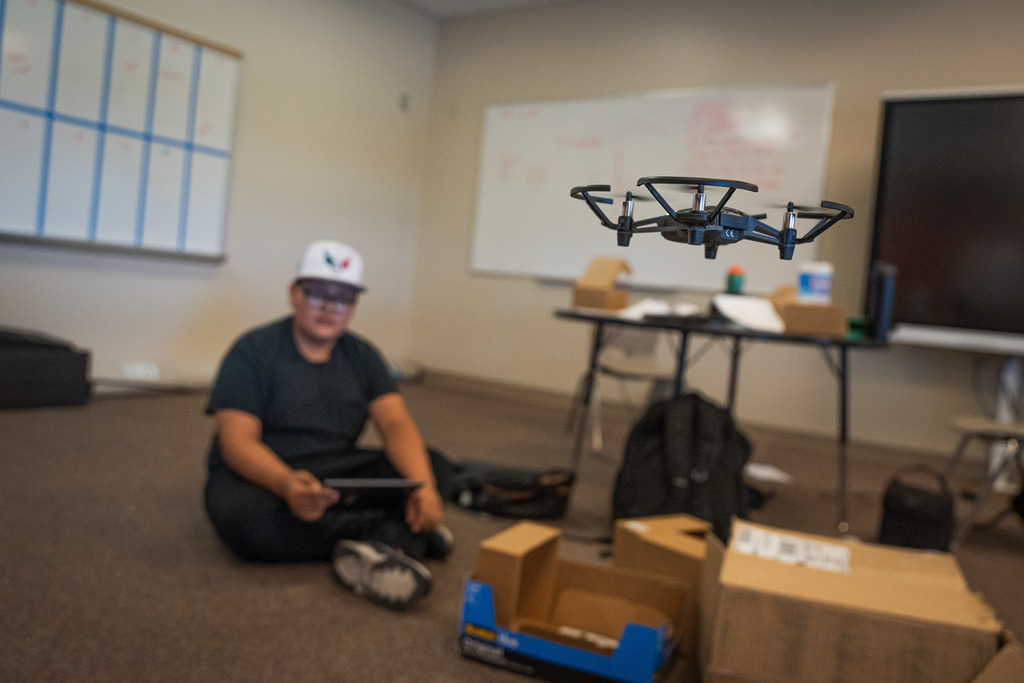 male student holding an ipad controlling a drone in the foreground